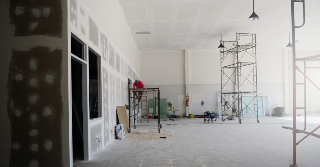 A large room that is unfinished. There is scaffolding and various pieces of equipment scattered throughout the room.